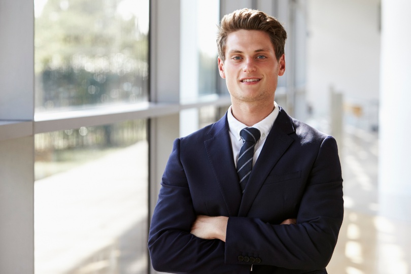 Professional young man in a suit standing confidently by a large window, representing expertise and reliability, ideal for showcasing Discord Community Management Services.